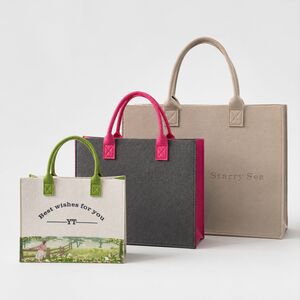 three felt bags in beige gray and white with green handles showcasing X-stitch detail and custom printing